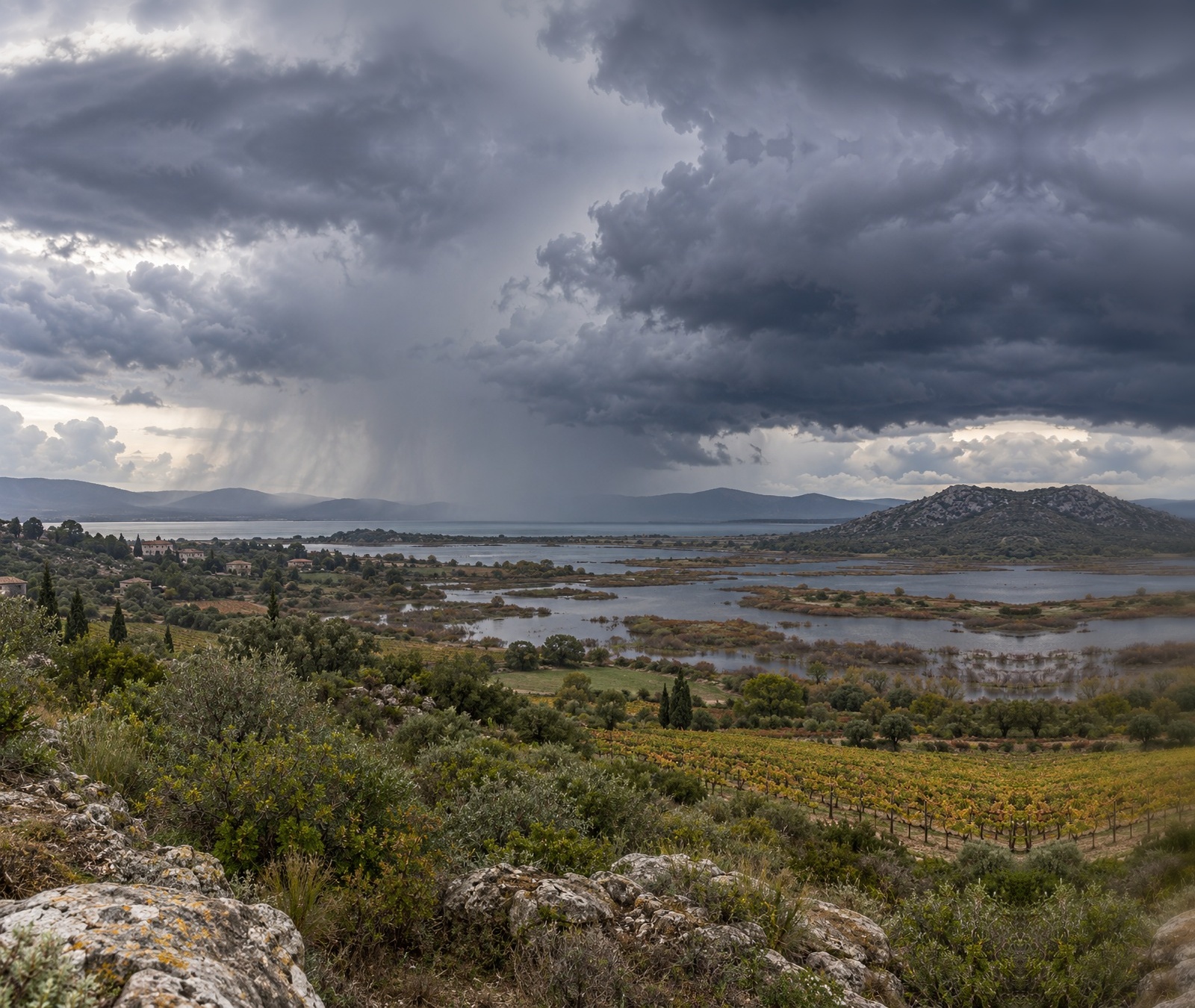 Paysage automnal du sud de la France sous un ciel chargé avec des averses au loin, image symbolique du temps plus instable près de la Méditerranée.