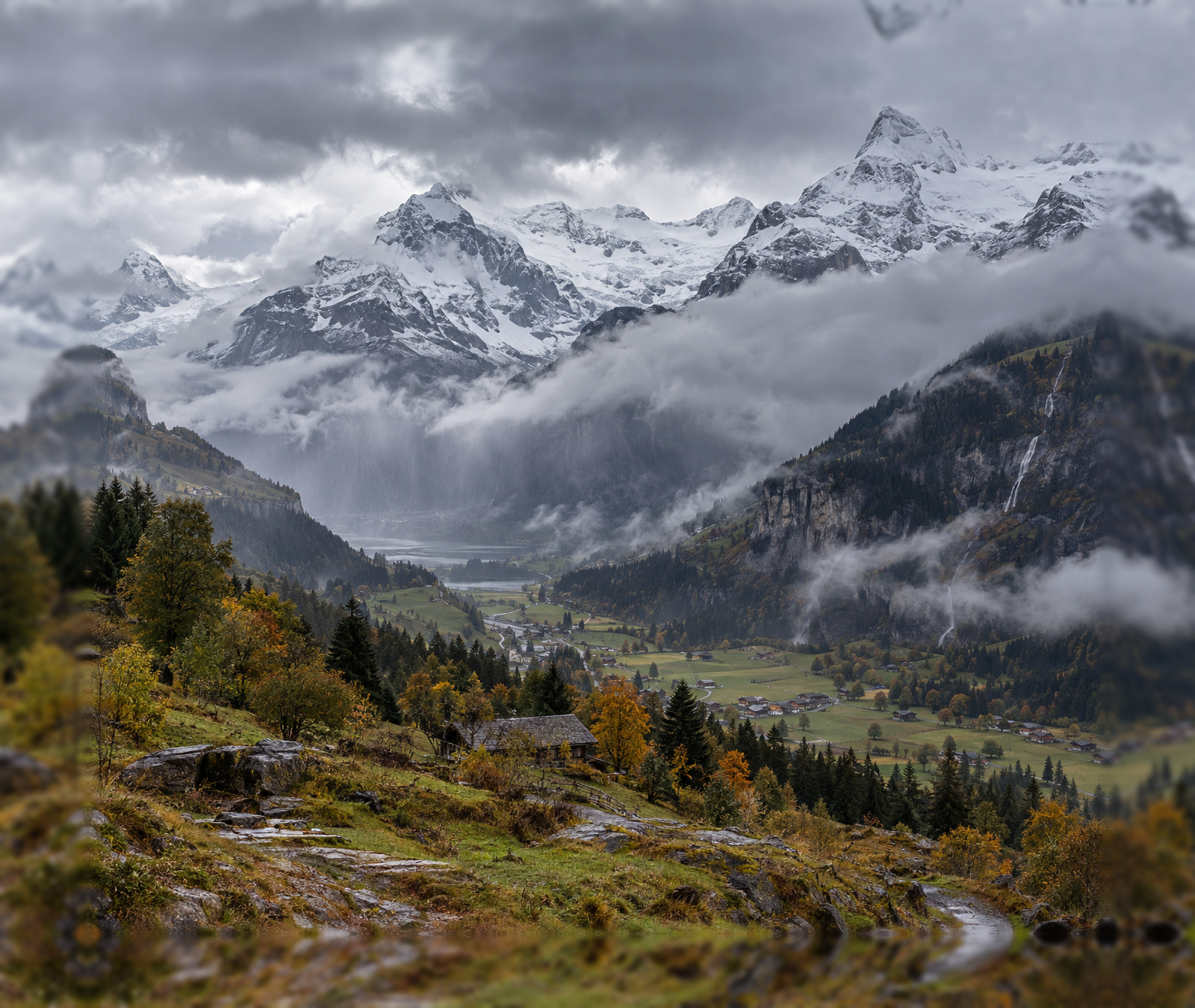 Vallée alpine française en automne sous la pluie avec neige fraîche sur les sommets.