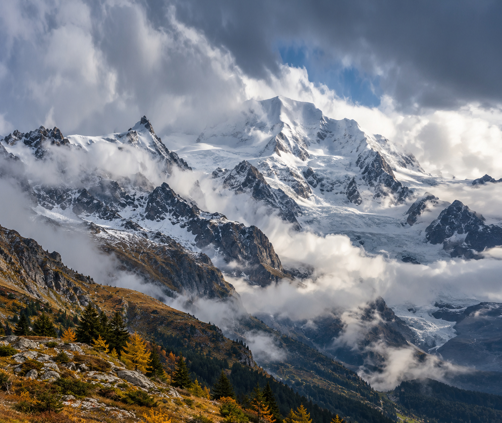 Image symbolique des Alpes françaises du Nord avec sommets fraîchement enneigés, brouillard et versants automnaux sous un front froid.